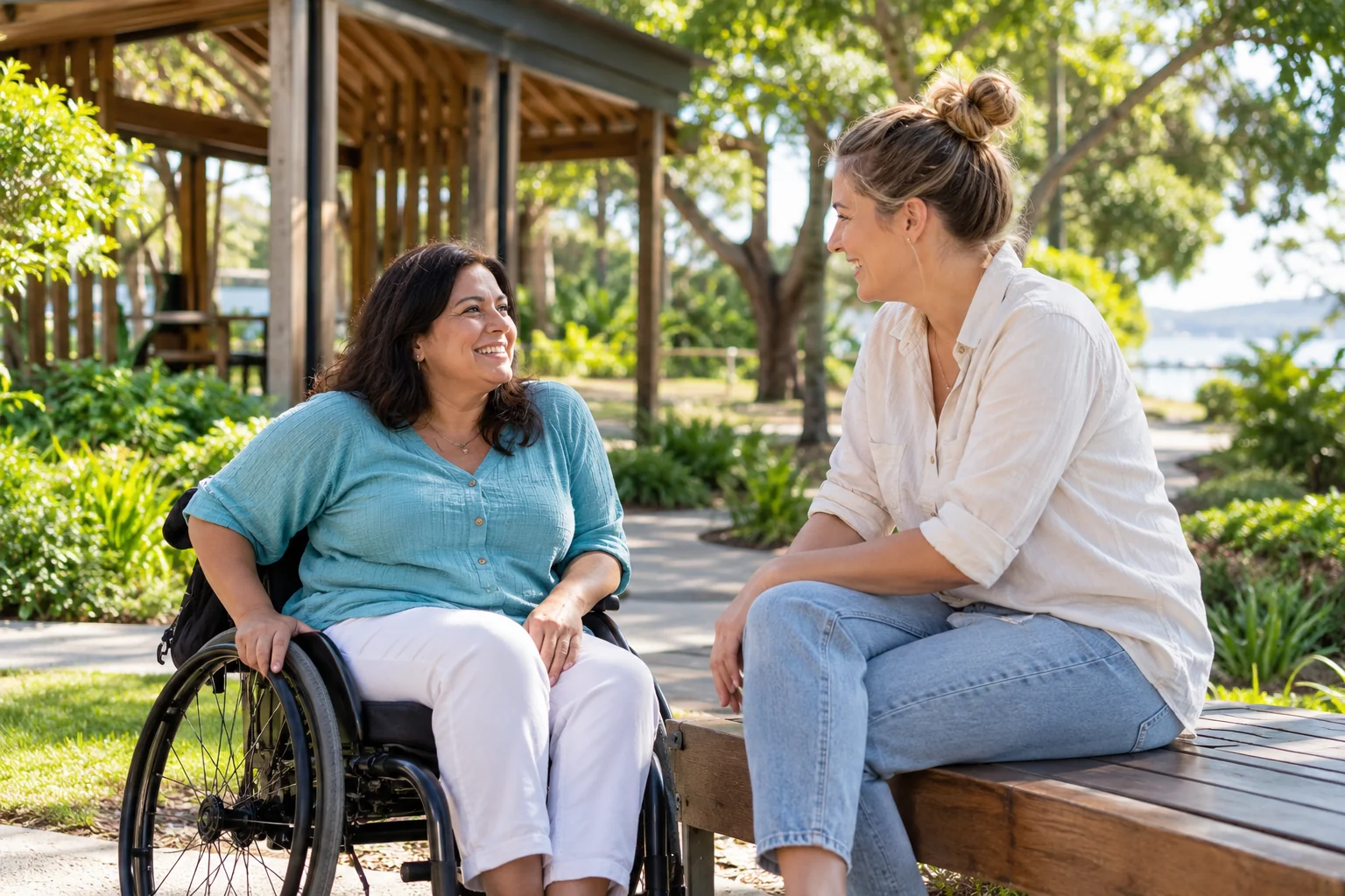 A woman using a wheelchair discussing NDIS support with a companion in a park